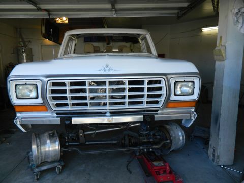 1979 Ford Bronco - Front view of a white 1979 Ford truck undergoing repairs in a garage, with its front suspension exposed.