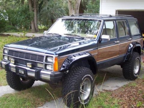 1984 Jeep Cherokee XJ with wood paneling and off-road tires parked outside a garage