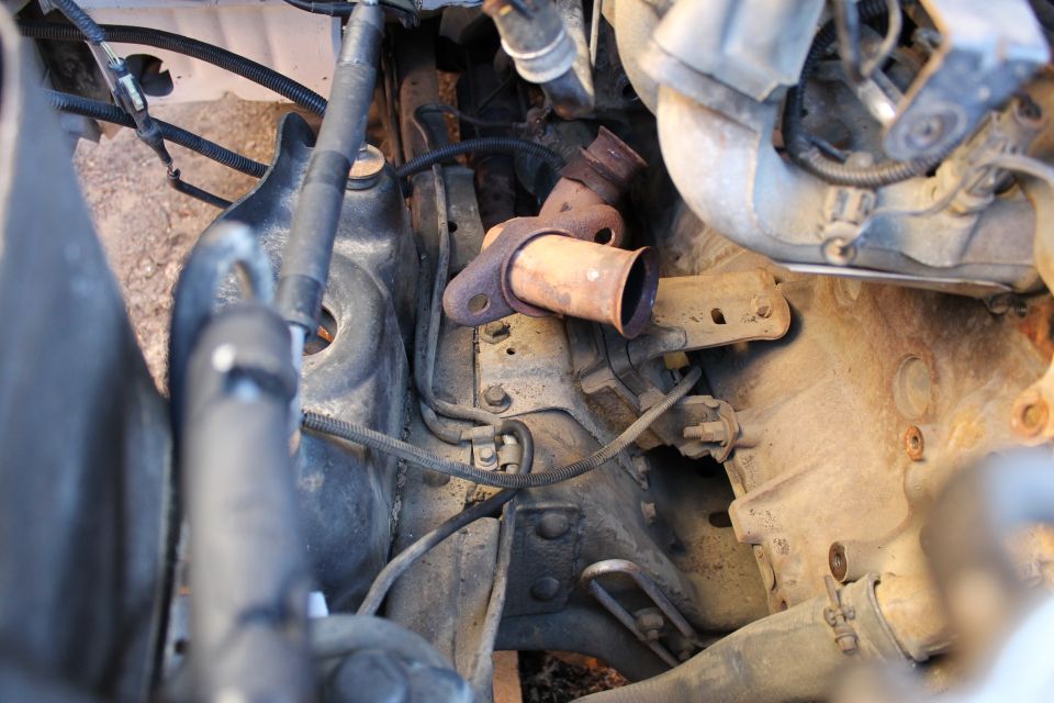 Rusty exhaust manifold outlet and brackets in a dirty engine bay