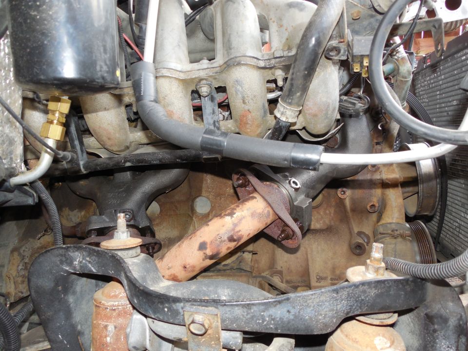 Cast-iron exhaust manifold with rusty outlet pipe on an EFI engine, viewed in the engine bay