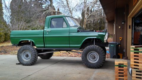 1967 Ford F-250 - A modified 1967 Ford F-250 pickup truck with a lifted suspension and large off-road tires sits outside a garage.