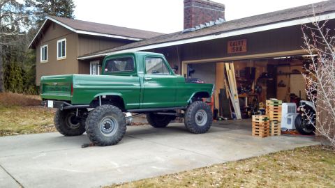 1967 Ford F-250 - A green pickup truck with oversized tires is parked in a driveway next to an open garage.