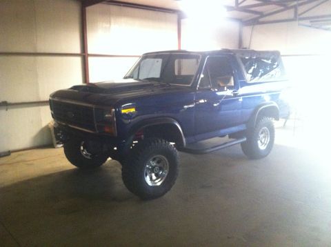 1982 Ford Bronco - Blue Ford Bronco with aftermarket hood scoop and lifted suspension is parked inside a garage.