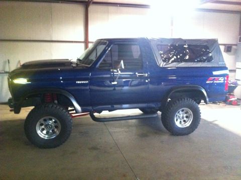 1982 Ford Bronco - Blue Ford Bronco with a lifted suspension and off-road tires is shown from the side in a garage.