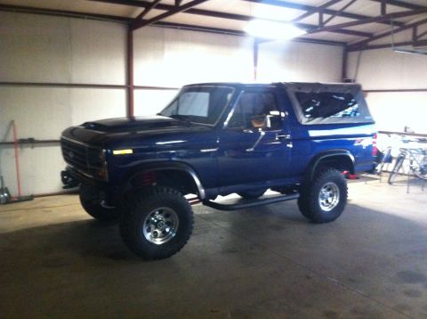 1982 Ford Bronco - Blue Ford Bronco with aftermarket hood scoop and soft top is parked in a garage.