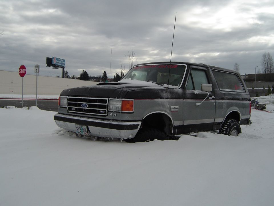 Snow-dusted Ford Bronco front, 4x4 fender badge, stop sign behind