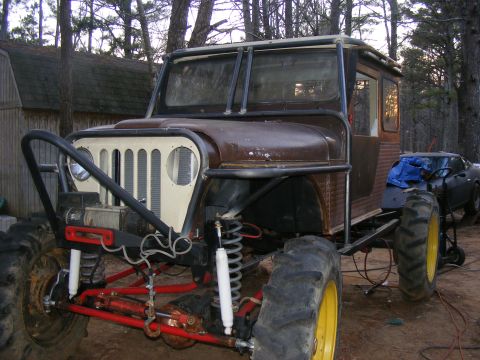 Modified Jeep CJ-5 with large tractor tires, custom roll cage, and winch. The vehicle is brown and has a white