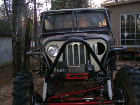 Customized Jeep CJ with large tires, roll cage, and winch. It has a beige grille and a black bumper