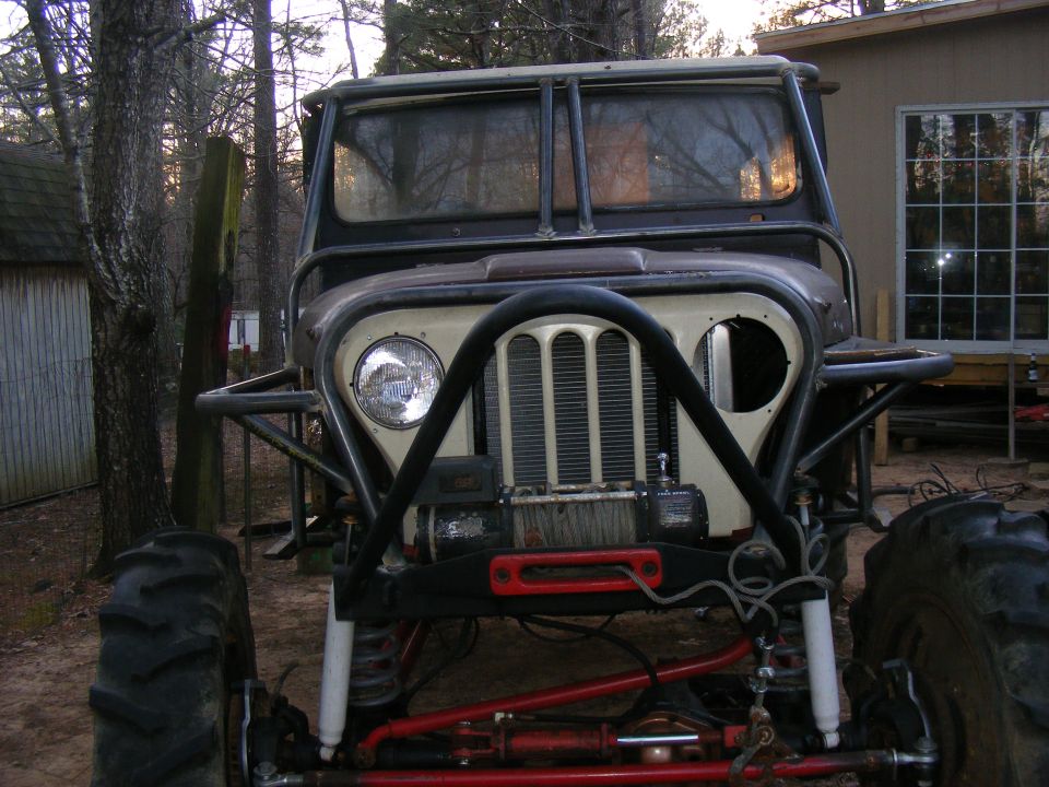 Customized Jeep CJ with large tires, roll cage, and winch. It has a beige grille and a black bumper