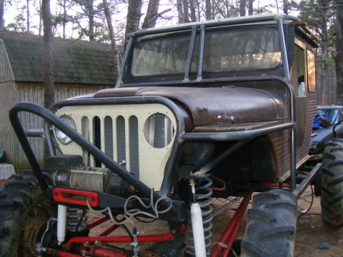 Custom Jeep with roll cage, winch, and large tires. It has a brown body and a cream-colored grille