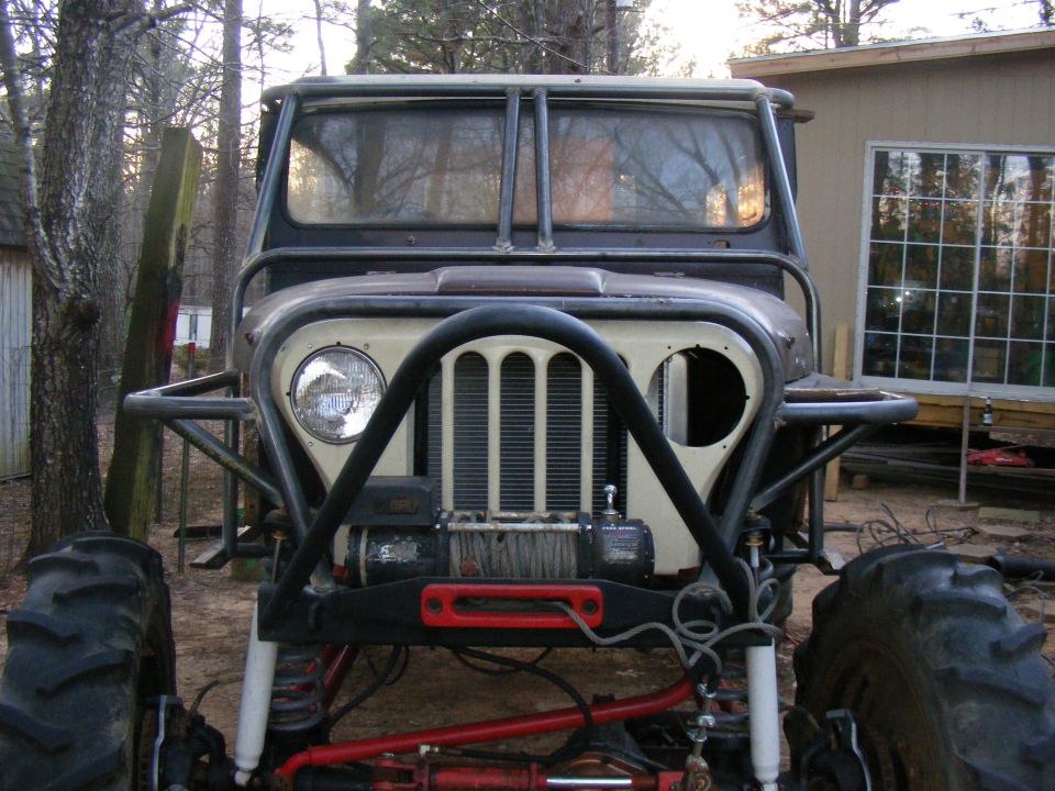 Modified off-road vehicle with large tires, winch, and custom roll cage, viewed from the front