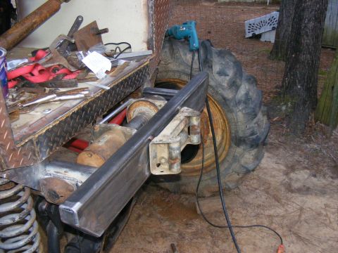 Close-up of a large tire and suspension components with tools and a drill nearby