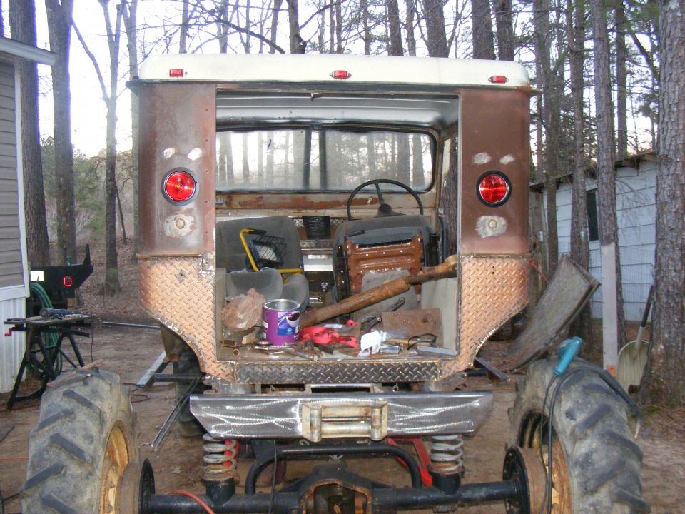Rear view of a heavily modified off-road vehicle with large tires, custom bumper, and open interior. It appears to be under construction