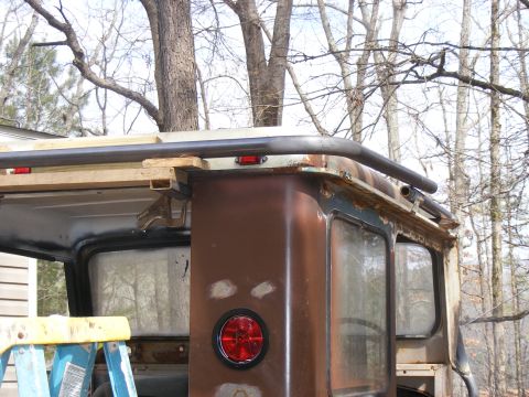 rear of rusty SUV with roll cage being installed, trees in background