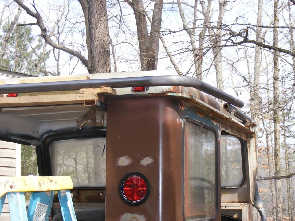 rear of rusty SUV with roll cage being installed, trees in background