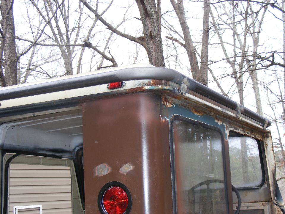 Close-up of a rusted vehicle's rear corner, showing a taillight and window frame