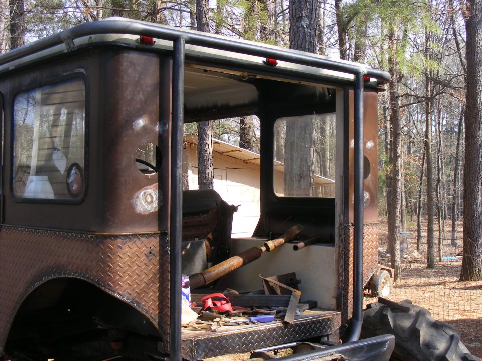 Custom off-road vehicle with roll cage, diamond plate accents, and exposed interior. Looks like it's in a wooded area