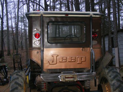 Rear view of a brown Jeep CJ-5 with a copper tailgate and large tractor tires