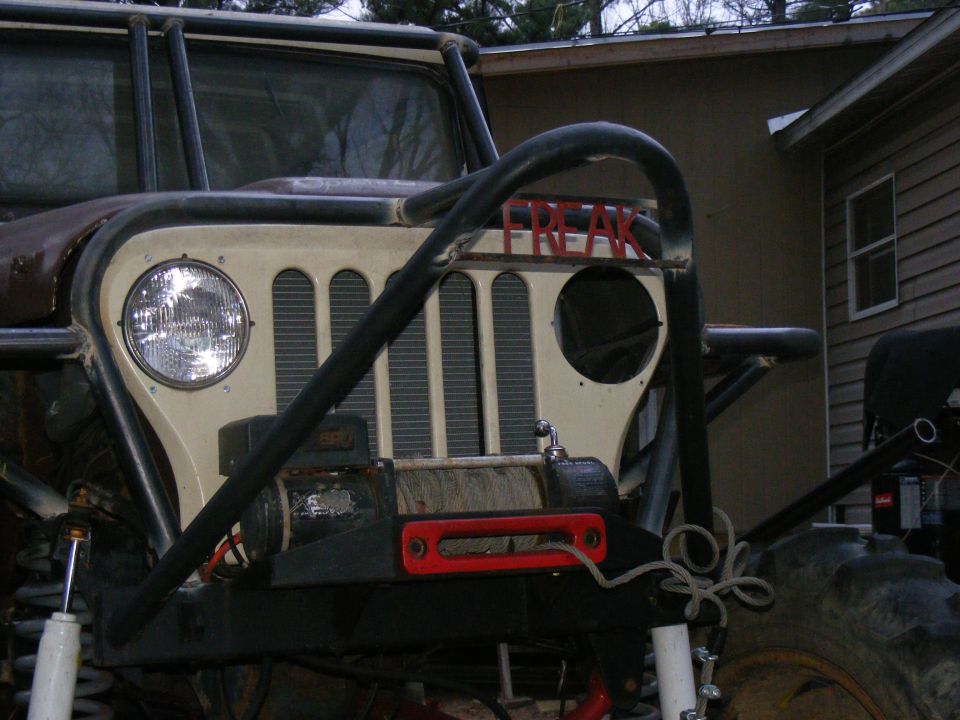 Modified off-road vehicle front end with a winch and a roll cage, painted "FREAK" on the grille