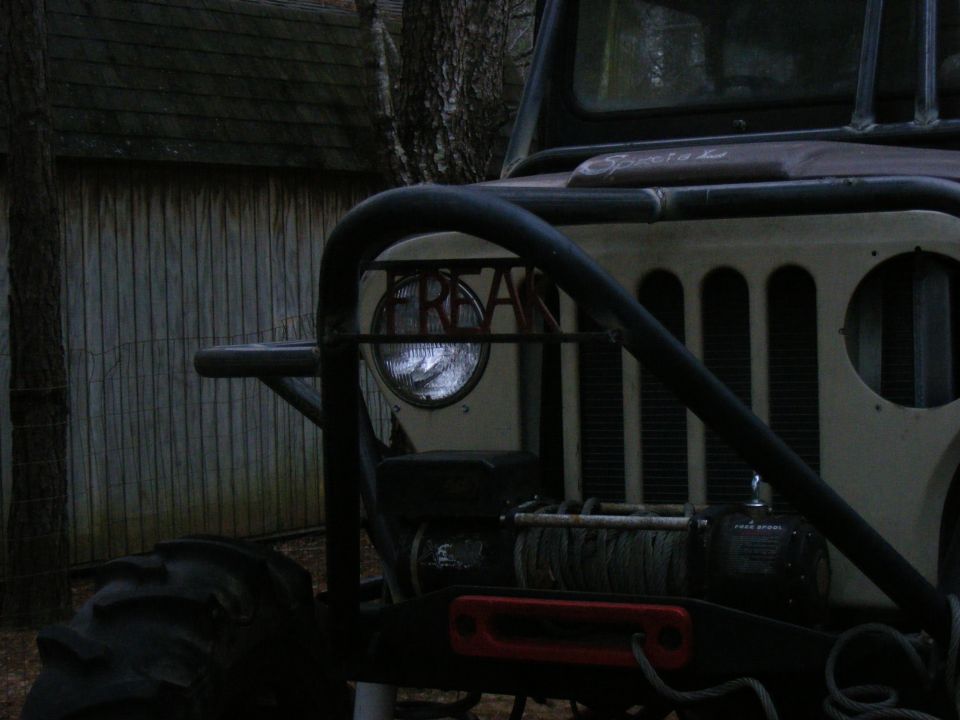 Front of a heavily modified Jeep CJ with a winch and roll cage. The word 'FREAK' is visible on the headlight