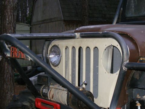 Off-road vehicle grille with vertical slots and a round headlight, protected by a black roll cage