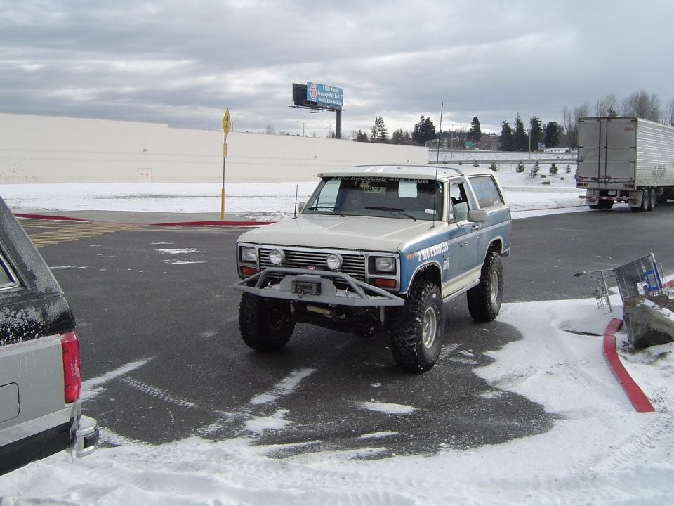 Lifted silver-and-blue Bronco with brush guard and winch in parking lot