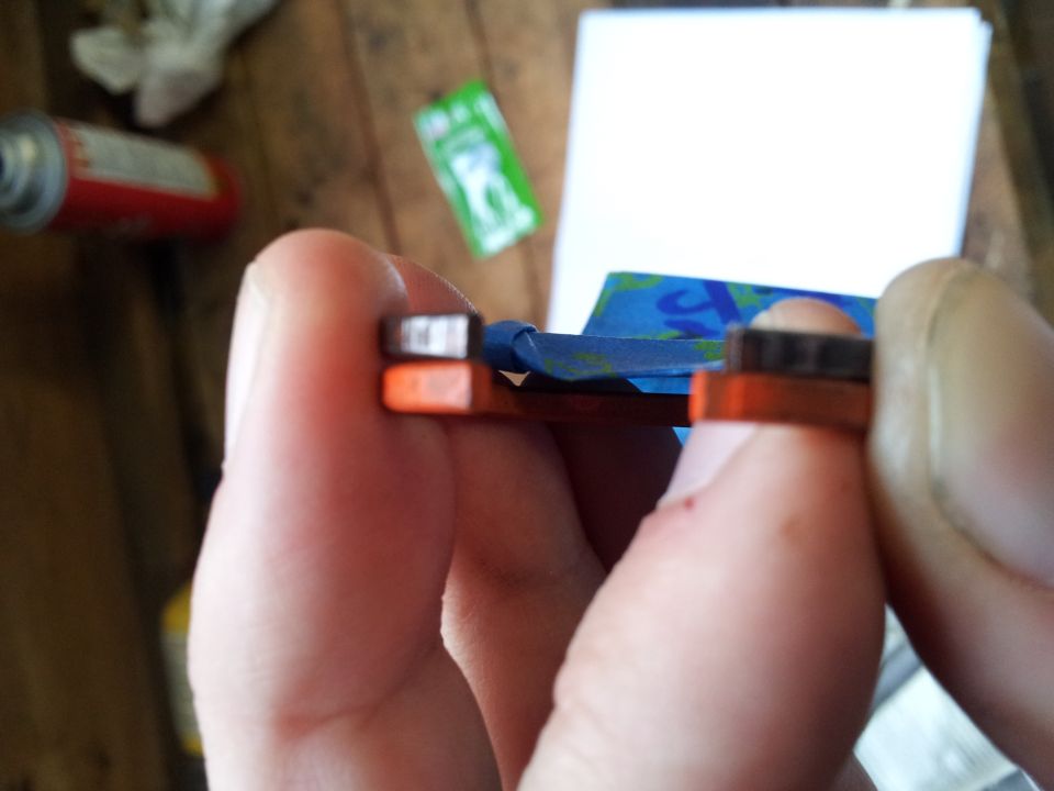 Close-up of hands holding a small orange and black automotive part with blue tape