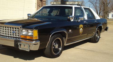 1991 Ford Crown Victoria LTD - A black and white 1991 Ford Crown Victoria LTD police car is shown from a three-quarter front view.