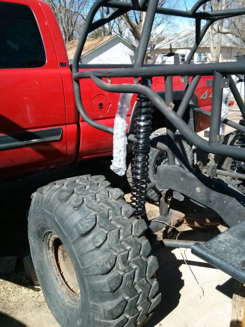 1986 Ford Bronco - Off-road buggy frame and large tire next to a red truck bed.