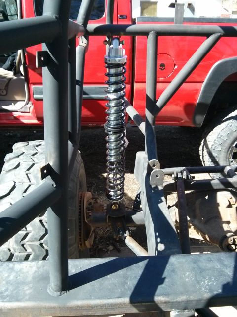 1986 Ford Bronco - Custom suspension system with a prominent coilover shock absorber is shown, with a red truck in the background.