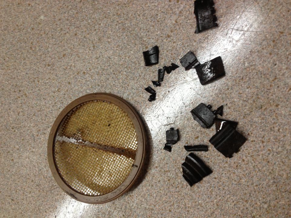 Broken air filter element and scattered black rubber fragments on a speckled surface