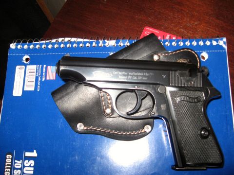 1992 Ford Mustang - A Walther PP pistol with a holster rests on a blue notebook, displaying text and an American flag sticker.