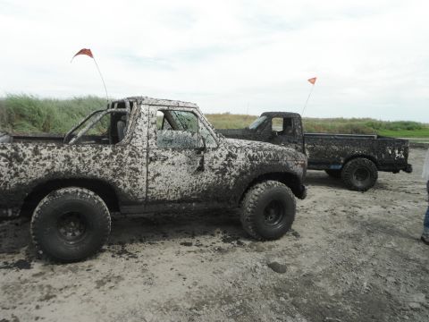 1980 Ford Bronco - Two off-road vehicles are heavily covered in mud after driving through a wet terrain.