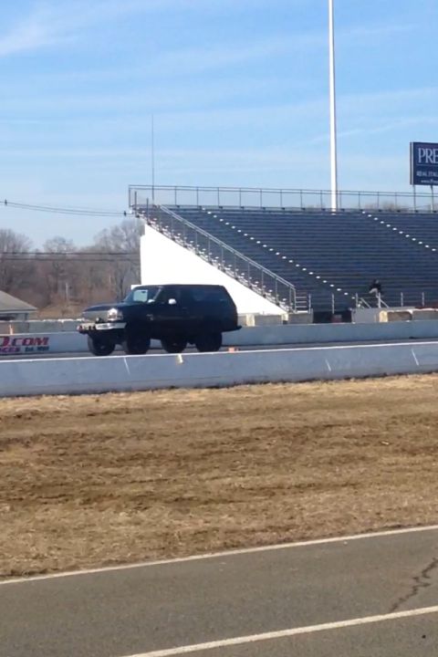 1995 Ford Bronco - A black SUV is positioned on a drag strip, with bleachers visible behind a barrier.