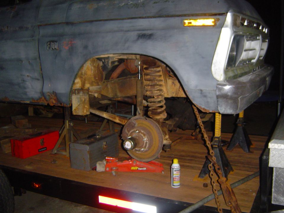 Ford F-150 truck body on jack stands, showing rusted wheel well and suspension components