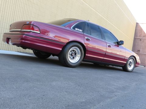 1992 Ford Crown Victoria - Low three-quarter rear view of a maroon Ford Crown Victoria sedan parked on asphalt beside a tan corrugated metal building, sitting on poli…