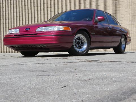 1992 Ford Crown Victoria - A maroon 1992 Ford Crown Victoria is shown from the front three-quarter view, parked on asphalt in front of a textured wall.