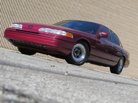 1992 Ford Crown Victoria - A maroon 1992 Ford Crown Victoria with distinctive Weld Magnum III wheels is shown from a low angle in front of a textured wall.