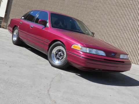 1992 Ford Crown Victoria - A maroon Ford Crown Victoria is parked on a concrete surface with a textured wall in the background.