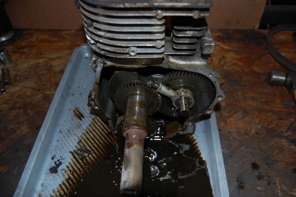 Engine with gears exposed, sitting in a drain pan with oil
