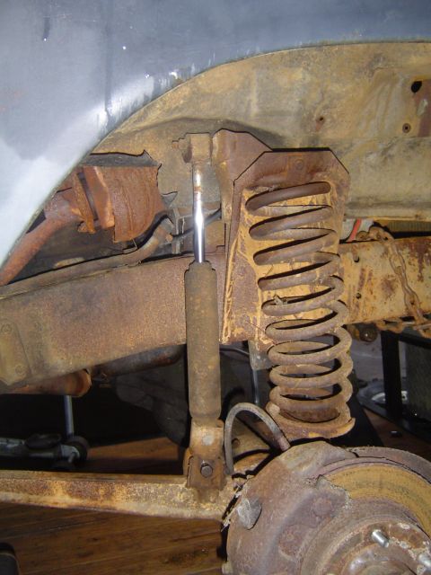 1986 Ford Bronco - Close-up view of heavily rusted suspension and brake parts on a vehicle.