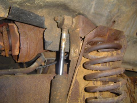 1986 Ford Bronco - Close-up of heavily rusted suspension parts, including a coil spring and shock absorber.