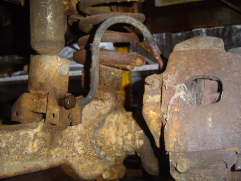 1986 Ford Bronco - Detail shot of heavily rusted suspension components, including a coil spring and brake caliper.