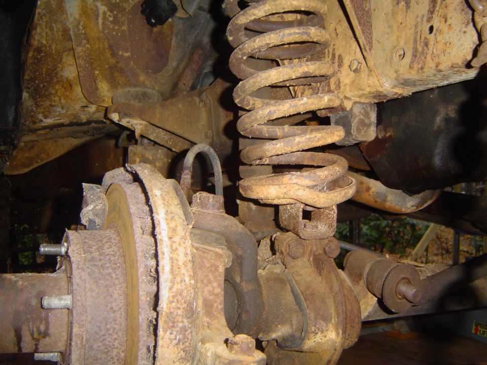 Close-up of heavily rusted front suspension parts, including a coil spring and brake rotor assembly