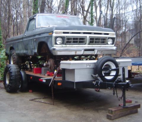 1986 Ford Bronco - A lifted Ford pickup truck is loaded onto a trailer, showing its front end and grille.
