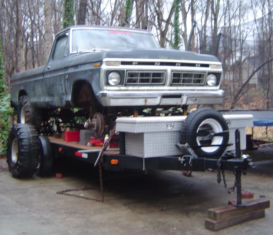 Ford pickup truck on a trailer, front view. Truck has a lifted suspension and large tires