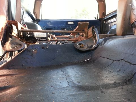1994 Ford Bronco - The interior floor of a vehicle is shown after a seat has been removed, revealing mounting hardware and the textured floor surface.