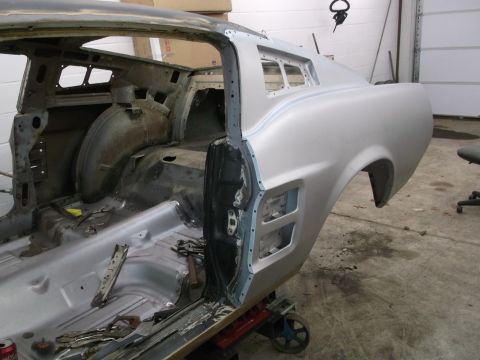 1967 Ford Mustang - The side profile of a silver 1967 Ford Mustang body is visible as it undergoes restoration, showing its interior structure.