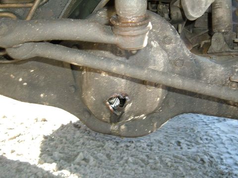1988 Ford Bronco - Close-up view of a damaged rear axle differential housing, revealing a hole and internal mechanics.