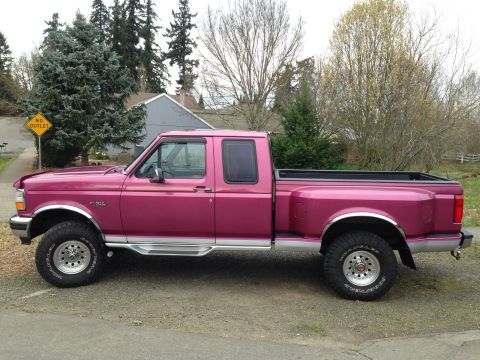 1992 Ford F-150 - A pink Ford F-350 Super Duty pickup truck is parked on a gravel surface with trees and a house in the background.